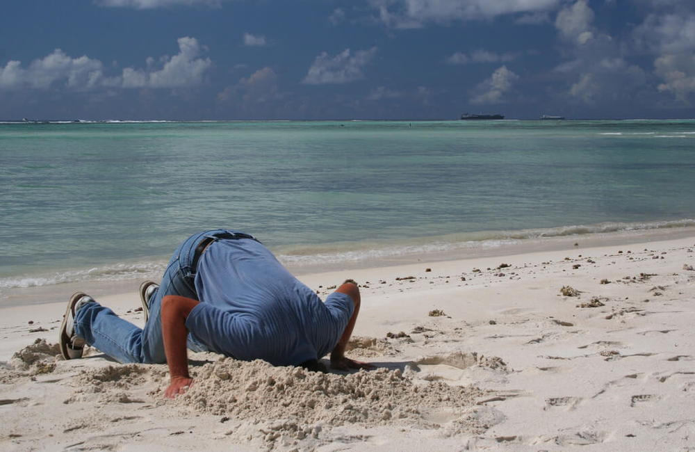 man burying head in sand - avoiding difficult situations